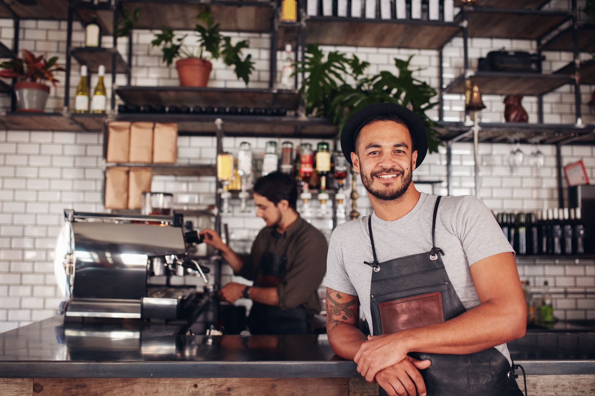 Business Home Summary Portrait of male coffee shop owner standing at the counter with barista working in background making drinks.