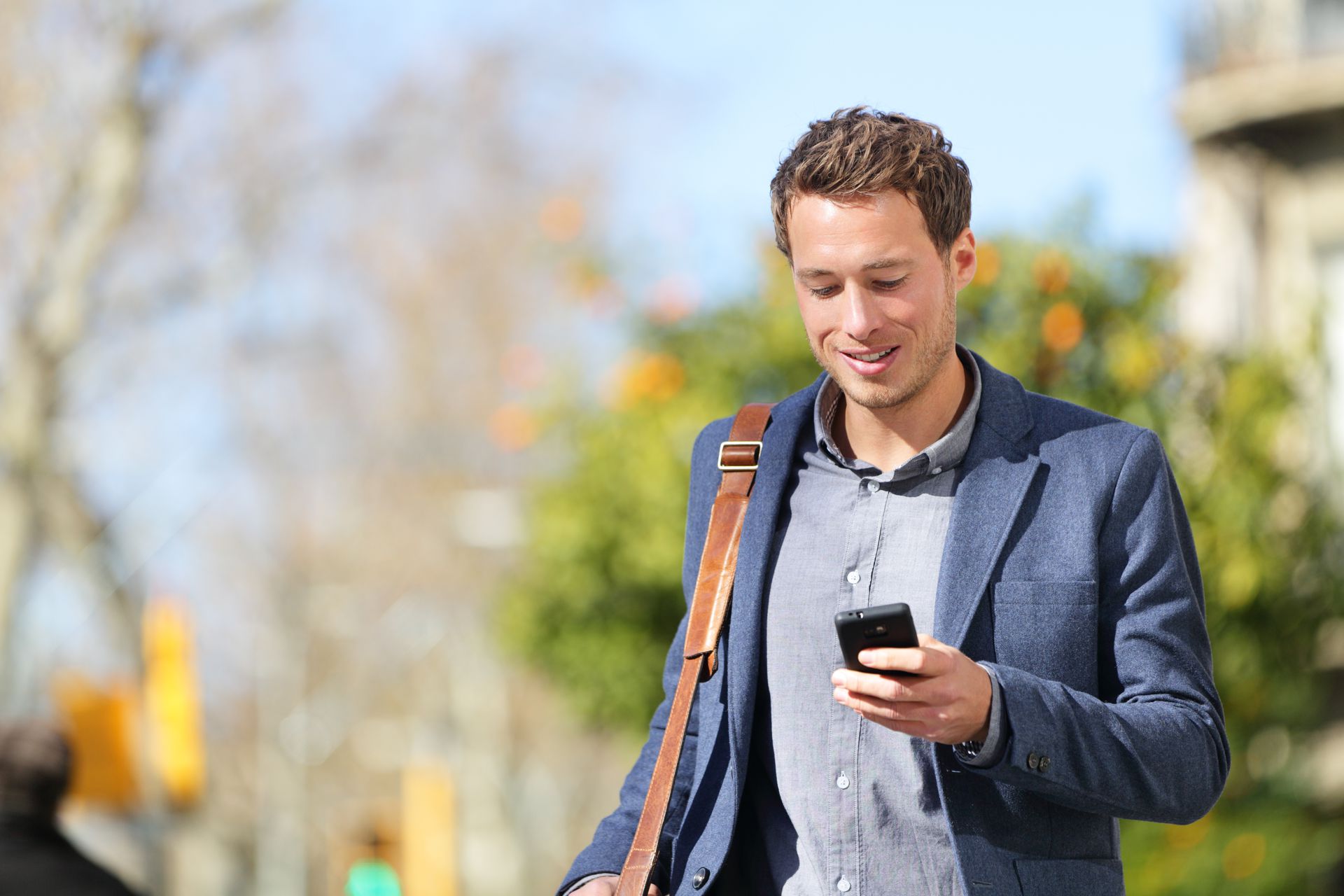 Business Security Manage from Anywhere Young urban businessman professional on smartphone walking in street using app texting sms message on smartphone wearing jacket on Passeig de Gracia, Barcelona, Catalonia, Spain.