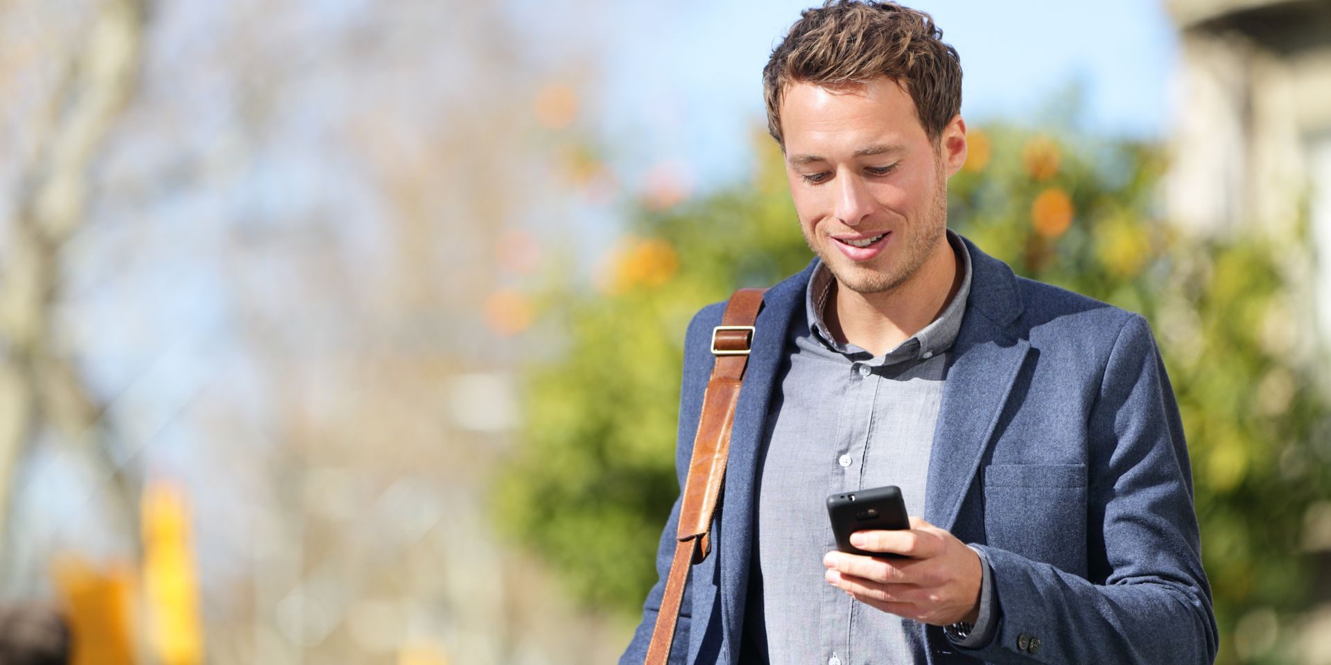 Young urban businessman professional on smartphone walking in street using app texting sms message on smartphone wearing jacket on Passeig de Gracia, Barcelona, Catalonia, Spain.